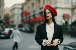 Moda mujer retrato en pie en el calle en frente de el ciudad en elegante ropa con rojo labios y rojo boina, viajar, cinematográfico color, retro Clásico estilo, urbano Moda estilo de vida. foto