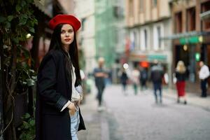 mujer Moda modelo camina en el calle en el ciudad centrar entre el multitud en un chaqueta y rojo boina y vaqueros, cinematográfico francés Moda estilo ropa, viaje a Estanbul foto