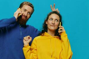 mujer y hombre alegre Pareja con Los telefonos en su manos torcido sonrisa alegre, en azul antecedentes. el concepto de real familia relaciones, hablando en el teléfono, trabajo en línea. foto