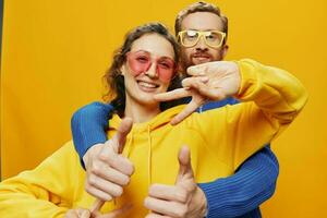 hombre y mujer Pareja sonriente alegremente y torcido con anteojos, en amarillo fondo, símbolos señales y mano gestos, familia disparar, recién casados. foto