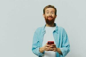 Man hipster with phone in hand blogger smile on gray background in blue shirt and white t-shirt, talking on the phone and selfies photo