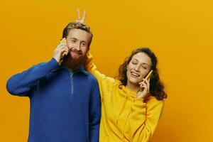 Woman and man cheerful couple with phones in hand talking on cell phone crooked smile cheerful, on yellow background. The concept of real family relationships, talking on the phone, work online. photo
