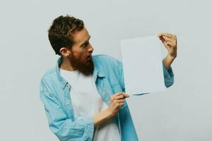 Portrait of an adult male on a gray background with a white sheet of paper in his hands for your design and text, layout, copy space, space for text, finger pointing photo