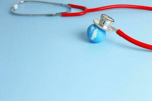 Checking health with red stethoscope on earth. World health day concept - blue earth with on light blue background. photo