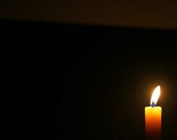 Close up single candle light and flame on black background photo