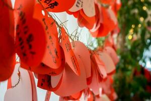 Otaru, Hokkaido, Japan 2018 - Closeup and crop Japanese lettering on wishing tags in red papers and heart shape hang on wire in LeTAO clock tower. photo