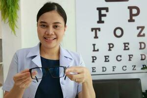 Female ophthalmologist holding eyeglasses inside clinic, eye doctor holding glasses in eyeglasses shop, Ophthalmologist holding eyeglasses in eyeglass clinic photo