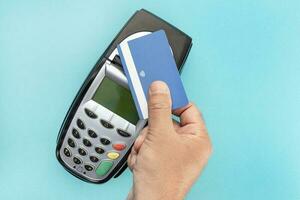 Hand make payment with credit card with NFC contactless technology on terminal device. Blue background photo