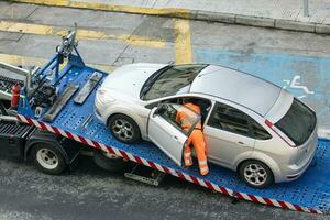 Damaged car being loaded onto tow truck by a worker. Towing service on the city. Roadside assistance concept photo