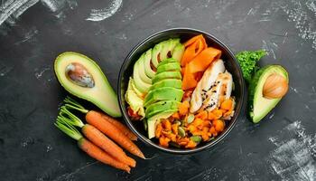 Bowl Buddha. Buckwheat, pumpkin, chicken fillet, avocado, carrots. On a black background. Top view photo