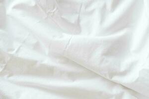 Abstract pattern of white crumpled bed sheet. White wrinkled fabric texture rippled surface. Close up. photo