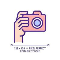 Hand with camera pixel perfect RGB color icon. Person taking shot with analog equipment. Photographer tool. Isolated vector illustration. Simple filled line drawing. Editable stroke