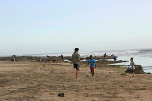 algunos pequeño niños jugando pelota en el arena playa con mar antecedentes. sur garut, Indonesia - julio 2023 foto