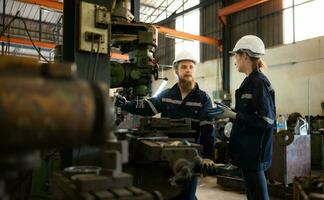 Both of mechanical engineers are checking the working condition of an old machine that has been used for some time. In a factory where natural light shines onto the workplace photo