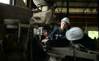 Both of mechanical engineers are checking the working condition of an old machine that has been used for some time. In a factory where natural light shines onto the workplace photo