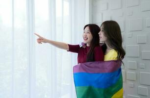 lgbt parejas cubrir arco iris banderas alrededor su amado unos a mantener calentar y mirada fuera su hotel habitación ventanas juntos. foto