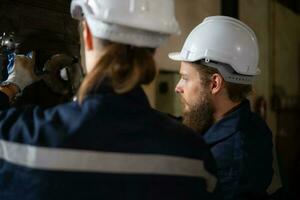 Both of mechanical engineers are checking the working condition of an old machine that has been used for some time. In a factory where natural light shines onto the workplace photo