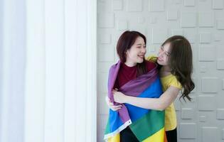 lgbt parejas cubrir arco iris banderas alrededor su amado unos a mantener calentar y mirada fuera su hotel habitación ventanas juntos. foto