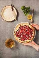 Hands putting strawberry galette on table served with plate and knife, herbal tea cup, honey and mint. Top view photo