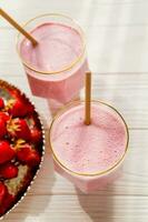 Fresh Milkshake or smoothie in glass with strawberries on wooden table, close up photo