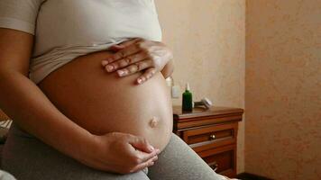 Close-up of the belly of pregnant woman, expectant mother gently caressing stroking touching her abdomen, relaxing, sitting on the bed at home. Happy pregnancy, procreation, maternity leave concept video