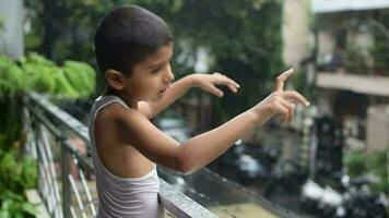 wenig Kind spielen im Sommer- Regen im Haus Balkon, indisch Clever Junge spielen mit Regen Tropfen während Monsun regnerisch Jahreszeit, Kind spielen im Regen video