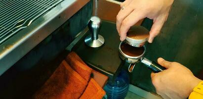 Close up barista's hand using tamper tool and grinder to make espresso shot in coffee maker machine at cafe photo