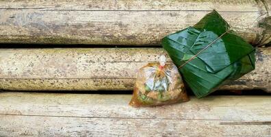 Plastic bag of spicy Stir fried chicken with basil and rice in wrapped banana leaves instead of dish on brown dry bamboo table with left copy space. Lunch, Natural material and Nature reserve photo
