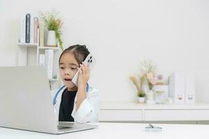 linda pequeño niña vistiendo del doctor Saco utilizando ordenador portátil foto