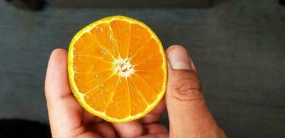 Close up hand and finger holding fresh half slice of orange with blurred grey or gray floor background. Healthy food and Fruit concept. photo