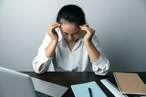 A business office worker is an asian woman is sitting in front of the laptop computer. A businesswoman stressing her body part fingers, hands arm. A femaleOffice manager is exhausted at her workplace. photo