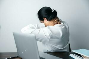 A business office worker is an asian woman is sitting in front of the laptop computer. A businesswoman stressing her body part fingers, hands arm. A femaleOffice manager is exhausted at her workplace. photo