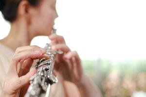 Asian woman wearing a cream colored dress She is playing the flute, an international wind instrument. Play classic songs. Performing concerts playing classical music in a band. music learning. photo