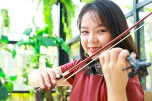 Asian woman playing classical instrument violin at home in the morning. She enjoys playing music. international music education concept Learning and practicing. Band and live music photo