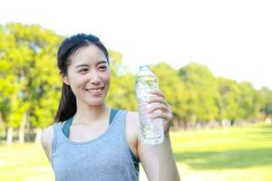 hermosa asiático mujer Bebiendo agua. ella ejercicios en un al aire libre parque. salud cuidado concepto al aire libre Deportes. Copiar espacio foto