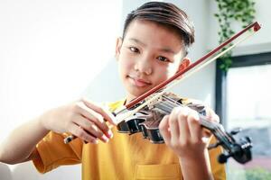 An Asian boy sits at home in the morning playing music. He was happily playing the violin of a classical instrument. Classical music concepts, develop learning, study and practice in childhood. photo