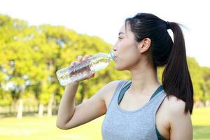 hermosa asiático mujer Bebiendo agua. ella ejercicios en un al aire libre parque. salud cuidado concepto al aire libre Deportes foto