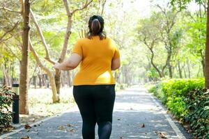 grasa asiático mujer vistiendo amarillo blusa trotar en el Mañana en el parque. concepto de peso pérdida ejercicio para el bueno salud de obeso gente. Copiar espacio foto