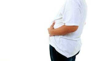 un grasa hombre vistiendo un blanco camisa retenida su barriga. en pie en un blanco antecedentes. peso pérdida conceptos, salud problemas de obeso gente. Copiar espacio foto