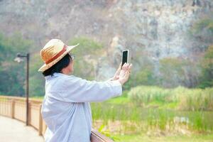 Asian elderly woman Traveling in nature, standing holding a smartphone, taking pictures of the rocky mountain scenery. Travel concept, happy retirement life, health care photo
