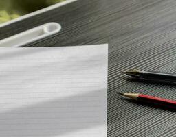 A blank paper, pen and pencil on a wooden textured table with partial shadows, after some edits. photo