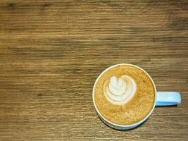 Latte topped with leaf-shaped milk froth and wood grain table photo