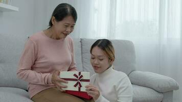 moeder dag, schattig Aziatisch tiener meisje geven geschenk doos naar volwassen midden- leeftijd mamma. liefde, kus, zorg, gelukkig glimlach genieten familie tijd. vieren speciaal gelegenheid, gelukkig verjaardag, gelukkig nieuw jaar, vrolijk Kerstmis video
