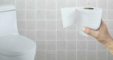 A person suffering from diarrhea holds a roll of toilet paper in front of the toilet bowl photo