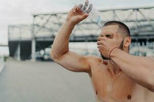 Athletic guy refreshes with water after intense workout, embraces sport, enjoys a healthy lifestyle. photo