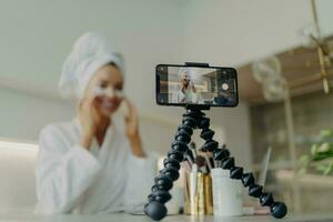 Beauty blogger records under-eye patch tutorial, tackles wrinkles and dark circles, focused on smartphone, bathrobe attire. photo