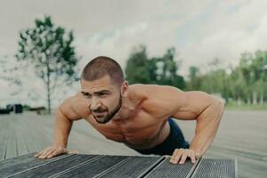 Active bearded man  shoulder, chest, biceps exercises. Good shape, outdoor poses. Muscled arms. Sport, workout, push-up concept. photo