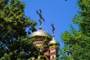 Dome of the Orthodox Church with crosses, view through the branches of trees against the blue sky photo