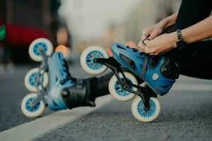 toma horizontal de una mujer sin rostro que se pone en patines en poses de carretera contra el fondo urbano involucrado en el deporte activo. gente hobby recreación deporte extremo estilo de vida activo concepto. foto