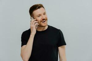 Satisfied ginger man talking on phone, receiving good news. Smiling, looking aside. Grey studio wall. photo